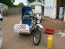 An off-road motorcycle fitted with knobbly mud tyres and a single sidecar, which has a cover over the passenger seat and a UNICEF logo on the front.