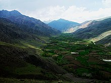 A lush green valley with a web of farm plots along the bottom.