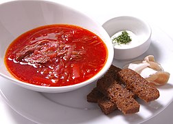 bowl of borscht with sticks of toasted brown bread and a small bowl of sour cream