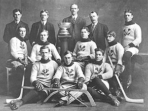 An early ice hockey team poses for a photo with a small championship trophy in the middle of them.