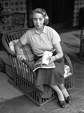 Photographie en noir et blanc d'une jeune femme assise sur un fauteuil en rotin.