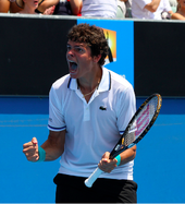 Raonic with his mouth open looks to the left, presumably to the crowd, and holds his racquet in his left hand.