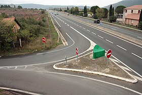 Vue diurne, en plongée (depuis un pont voisin), de l'ancien bâtiment voyageurs de la gare Salelles-du-Bosc (sur la gauche), jouxté par la bretelle de sortie à angle droit de l'autoroute.