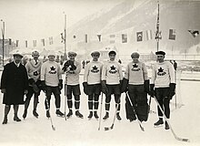 Black and white photo of a hockey team outside on natural ice, including a coach dressed in a dark overcoat, and seven players dressed in hockey equipment white sweaters with a maple leaf crest