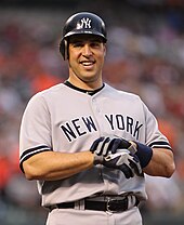 Mark Teixeira, wearing a dark blue baseball batting helmet and grey baseball uniform with the words NEW YORK across, takes off his batting gloves