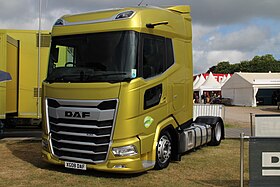 A yellow low-deck next generation DAF XG in a DAF stall at a truck show. It is a 2-axle chassis with dual tyres on axle two and a high capacity fuel tank.