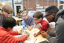 Five middle school students work together at a table using a soldering iron