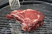 A raw ribeye steak placed on a grill