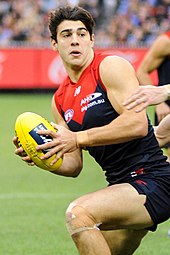 Male athlete in sleeveless guernsey runs holds football