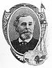 Head of a white man with a bushy goatee and thinning hair, wearing a dark suit coat and tie.