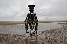 A bell in a complex wooden framework, on the beach at the edge of the sea