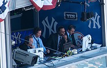 Wide shot of the Yankees television broadcast booth with Michael Kay to the left, Paul O'Neill and Ken Singleton in the center, and Ryan Ruocco to the right.