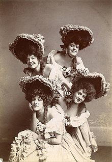 Four young white chorus girls, wearing bonnets and bouffant wigs or coiffures.