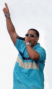 A man with sunglasses and a blue shirt holding a microphone.