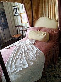 Four poster bed with pink sheets and a cream headboard.