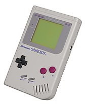 An original model Game Boy, a white, brick-shaped handheld. The upper half has a green screen surrounded by a gray border. The bottom half has a D-pad on the left, A and B buttons on the right, and Start and Select buttons in the middle.