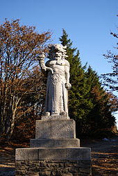 Statue entourée d'arbres, représentant un homme torse nu, aux cheveux longs, avec un casque cornu