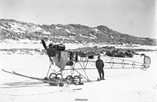 Un avion dont l'armature est visible posé sur la banquise, avec un homme à côté.