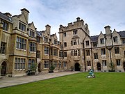 Grass lawn with small statue in centre, surrounded by neo-Gothic stone buildings with Elizabethan bay windows