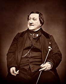 Rossini wears a vest and overcoat, holding a cane and looking out of frame