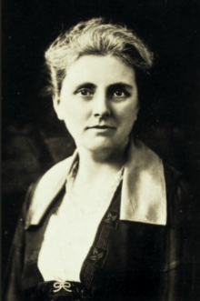 B&W portrait photo of a woman with her hair in an up-do, wearing a white-collared dark blouse.