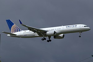 A mostly white Boeing 757 with blue and yellow trim preparing for landing against a grey sky.