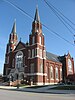 A brick church building with twin steeples, highlighted against a blue sky