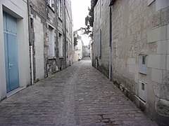 Photographie en couleurs d'une rue pavée, vue en enfilade entre deux deux rangées de façades.