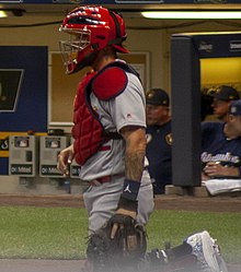 A baseball player walks in from the bullpen in his catcher's gear.