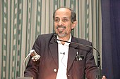 A photograph of a man standing in front of a microphone