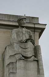 Stone statue of a seated man splitting a block of slate with a chisel