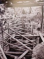 Photographie noir et blanc montrant un groupe d'ouvriers devant une large tranchée très fortement étançonnée.