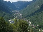 Foto auf eine langgestreckte Siedlung in einem Tal hinab. Die Siedlung liegt an einem Fluss und ist von Bergen umgeben.