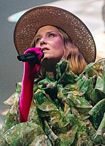 A woman with colorful hat and dress singing pop music