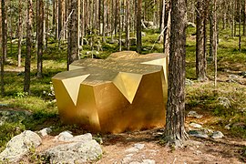 Bloc doré en forme d'étoile à six branches situé dans une forêt de conifères.