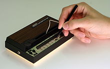 Photo d'un petit clavier électronique sur lequel une main appuie à l'aide d'un stylet