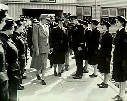 Two rows of women in dark military uniforms facing each other, with other military personnel and one civilian walking between them