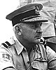 Informal portrait of a Caucasian man in light-coloured military shirt with peaked cap, and pilot's wings on left-breast pocket
