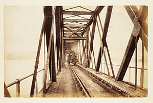 Sepia colourted photograph of the section of the first Tay Bridge before its collapse. A steam train is crossing the bridge.