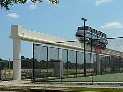 A white and blue monorail looking vehicle sitting on metal track on a concrete beam. The photo is grainy and washed out.
