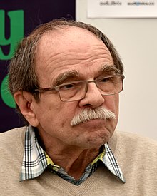 older white man with a moustache, wearing glasses, looking left of camera