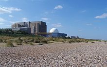 Nuclear power station next to shingle beach. A large factory-like concrete building with a prominent white dome in front.