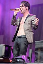Brendon Urie performing onstage in a brown jacket.