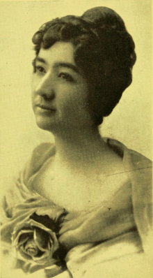 B&W portrait photo of a middle-aged woman with an up-do wearing a fancy top.