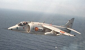 A Harrier flies over an aircraft carrier below.
