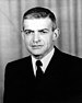 Head and shoulders of a white man with short hair neatly combed, wearing a dark suit coat and tie.