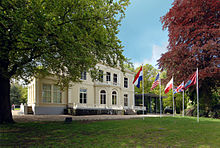 White building with law in front and flagpoles with flags flying