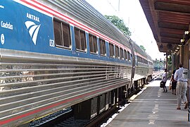Stainless steel passenger rail cars with a blue stripe and two thinner red stripes at window level, plus a red sill stripe