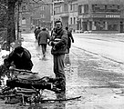 One man gathers branches for firewood, another cradles precious loaves of bread.