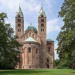 Looking toward the choir of a brick Romanesque cathedral. The twin bell towers, the transept crossing dome, and the roof are green copper